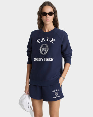 Person wearing a navy 'Yale Sporty & Rich' sweatshirt and shorts on a white background