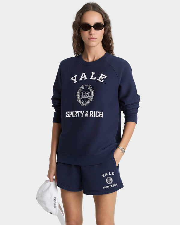 Person wearing a navy 'Yale Sporty & Rich' sweatshirt and shorts on a white background