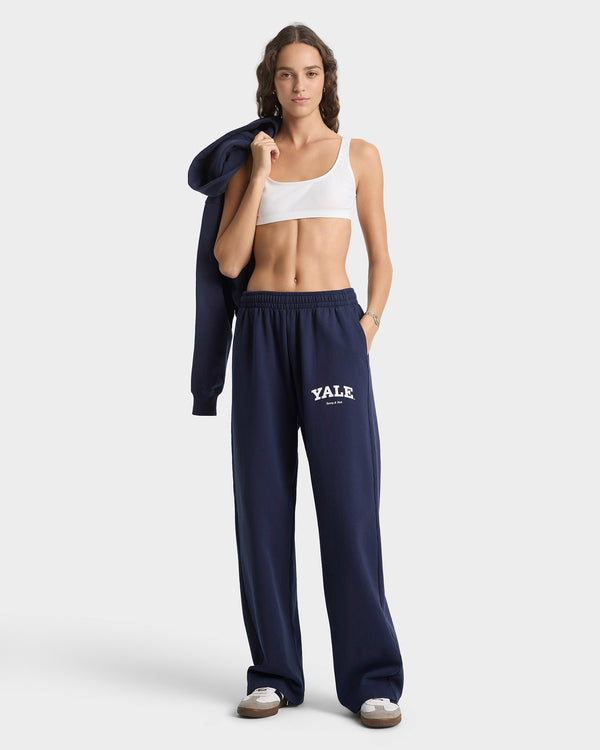 Woman wearing navy Yale sweatpants and a white crop top on a white background