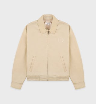 The H&W Crest Prep Jacket in cream is a relaxed-fit cotton twill layer with a collar, metal zip closure, front pockets, and a subtle embroidered logo on the left chest.