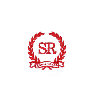 The Golf Logo Kelly Skirt - White/Bright Red features a red laurel wreath with SR in the center and Sporty & Rich Club ribbon below, set against a white background and crafted from high-quality fabric for a polished appearance.