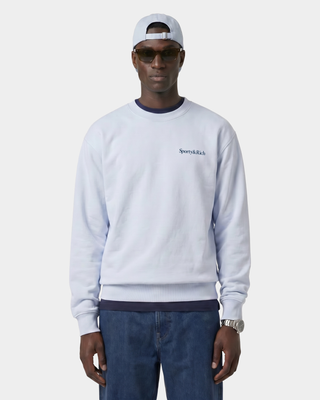 Man wearing a light gray sweatshirt with a brand logo, dark sunglasses, and a white cap on a white background.
