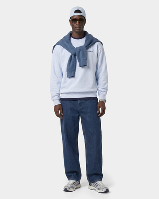 Man wearing a light blue sweater, dark blue scarf, and jeans on a white background