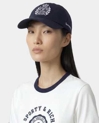 Person wearing a navy cap and white shirt with 'Sporty & Rich' branding on a light gray background