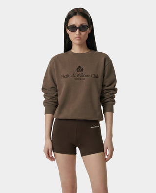 Person wearing a brown 'Health & Wellness Club' sweatshirt and shorts on a white background