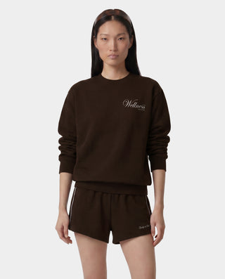 Woman wearing a brown sweatshirt and shorts set with 'Wellness' text on a white background