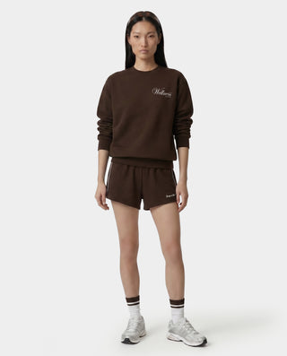 Person wearing a brown sweatshirt and shorts set with 'Wella' branding on a white background
