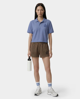Person wearing a blue polo shirt and brown shorts holding a water bottle on a white background