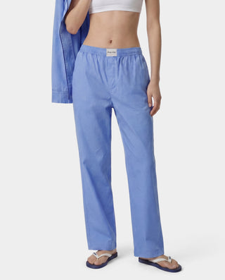 Person wearing blue pajama pants and a white top on a plain background