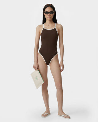Woman wearing a brown swimsuit holding a beige bag on a white background
