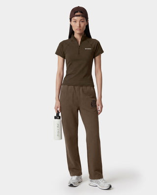 Person wearing a brown outfit with a logo, holding a white bottle on a white background