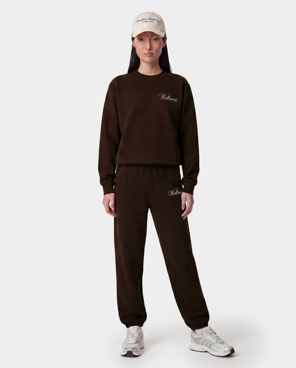 Person wearing a brown sweatshirt and pants with a logo, standing against a white background