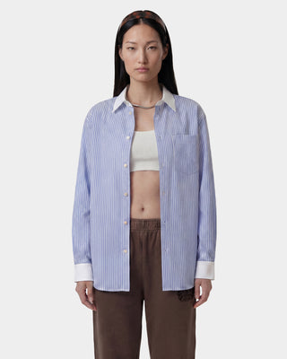 Woman wearing a blue striped shirt over a white top with brown pants on a white background