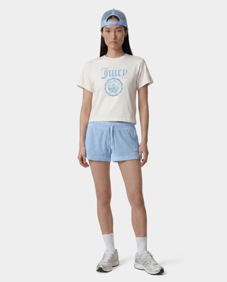 woman wearing a 'Juicy' t-shirt, light blue shorts, and cap on a white background