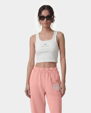 Woman wearing a white tank top and pink pants with logos on a white background