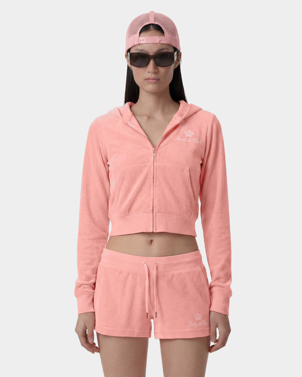 woman wearing a pink hoodie and shorts set with a cap and sunglasses on a white background