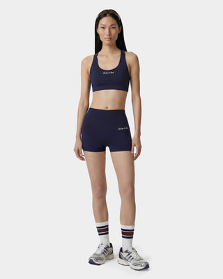Woman wearing a navy sports bra and shorts set with white socks and sneakers on a white background