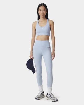 Woman wearing a light blue athletic outfit with a sports bra and leggings, holding a cap.