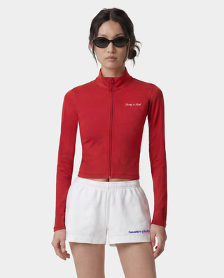 Person wearing a red jacket and white shorts with visible branding on a white background