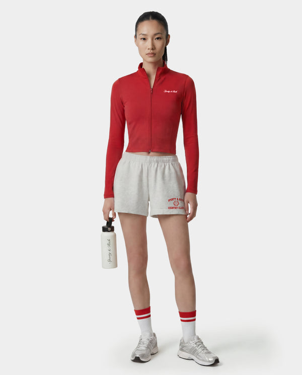 Person wearing a red athletic jacket and white shorts with a visible brand logo, holding a water bottle.