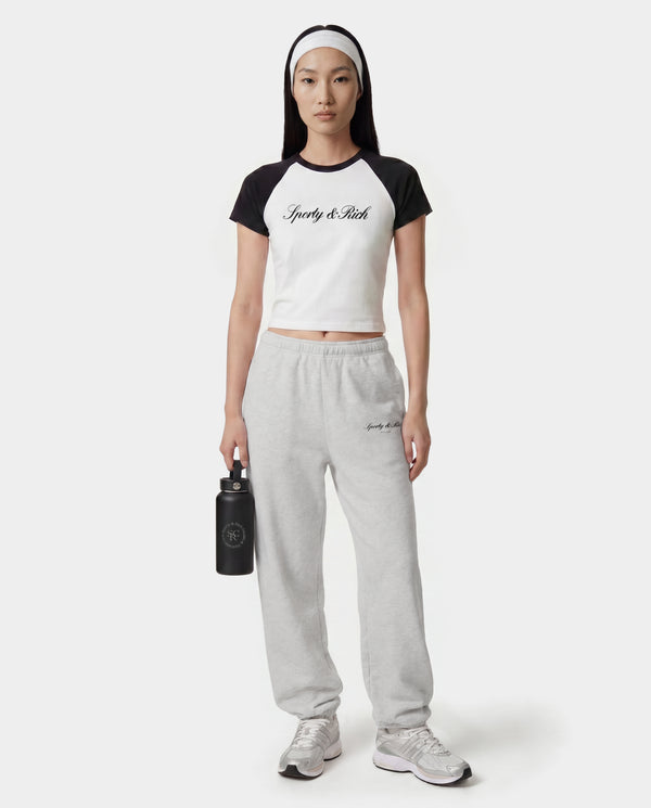 Person wearing a black and white t-shirt and gray sweatpants with a brand logo, holding a black water bottle on a white background.