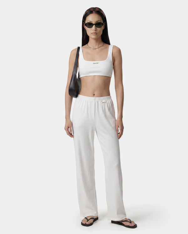 Woman wearing a white crop top and pants with a black bag on a white background
