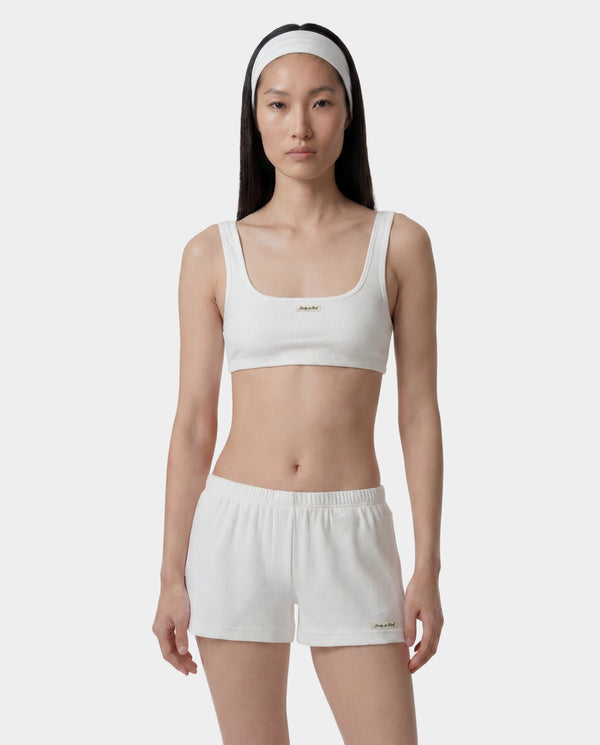 Woman wearing a white sports bra and shorts set on a plain background