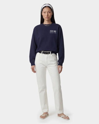 Person wearing a navy blue sweatshirt with a logo and white pants on a white background
