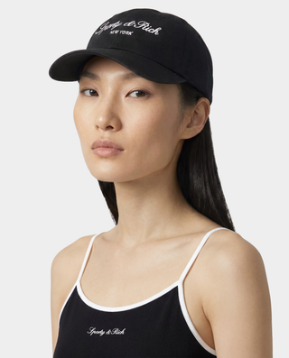 Woman wearing a black cap and black top with white trim, featuring a brand logo.