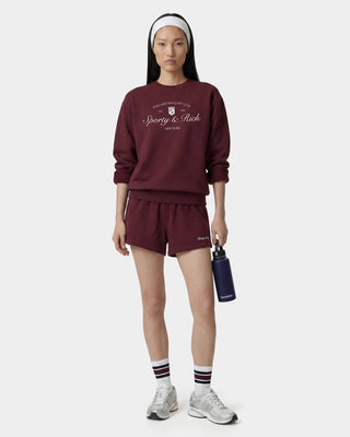Person wearing a burgundy sweatshirt and shorts with 'Sporty & Rich' branding on a white background