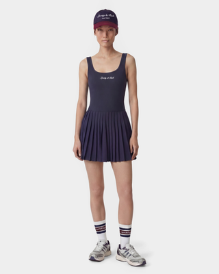 woman wearing a navy tennis dress with a matching cap and socks on a white background