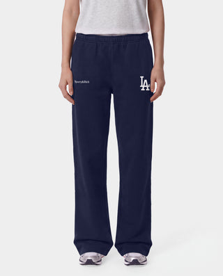 The LA Serif Wide Sweatpant in Dark Navy/White features a wide-leg, oversized fit crafted from 100% cotton and showcases a white LA logo along with Sporty & Rich text on the front, displayed lying flat on a white background.