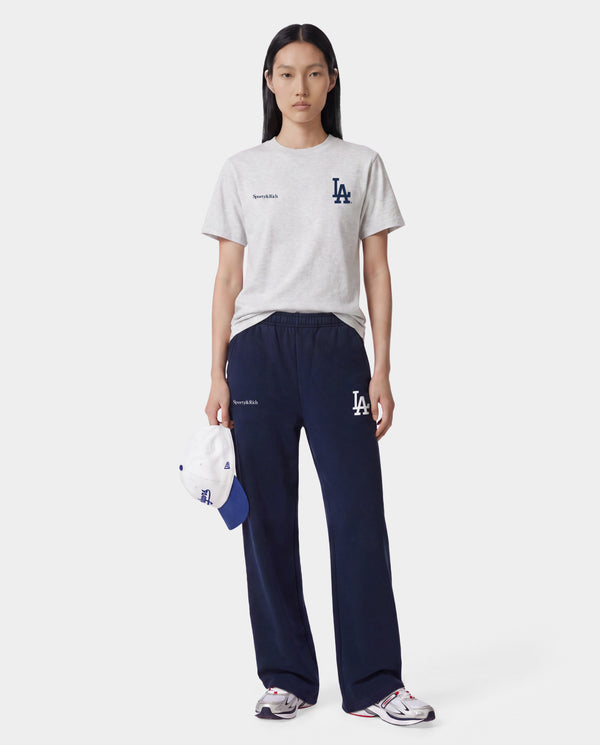 The LA Serif Wide Sweatpant in Dark Navy/White features a wide-leg, oversized fit crafted from 100% cotton and showcases a white LA logo along with Sporty & Rich text on the front, displayed lying flat on a white background.