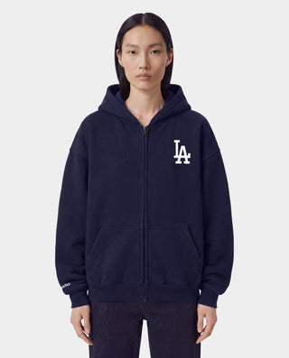 The LA Serif Zip Hoodie in Dark Navy/Navy features a zip front, LA logo on the left chest, and front pockets. Made from 100% cotton for comfort, this oversized hoodie is shown on a white background.