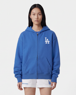 LA Serif Zip Hoodie in Team Blue/White, featuring a white LA logo on the left chest, front pockets, and a zip closure. Crafted from 100% cotton with an oversized fit and displayed laid flat on a white background.