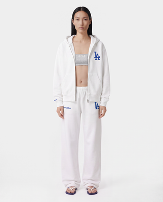 The LA Serif Zip Hoodie - White/Navy features a white zip-front design, crafted from 100% cotton, with a blue LA logo on the left chest and a front pocket, displayed against a plain background.