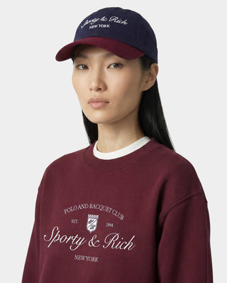 women wearing a burgundy sweatshirt and cap with 'Sporty & Rich' branding on a white background