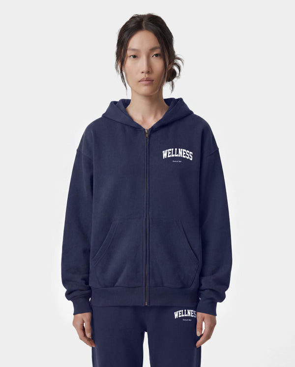 Wellness Ivy Zip Hoodie in Dark Navy/White—crafted in Portugal from 100% cotton, featuring a white WELLNESS print on the left chest and a zip-up hooded design.