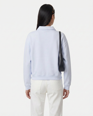 women wearing a light blue sweater and white pants with a black bag on a white background