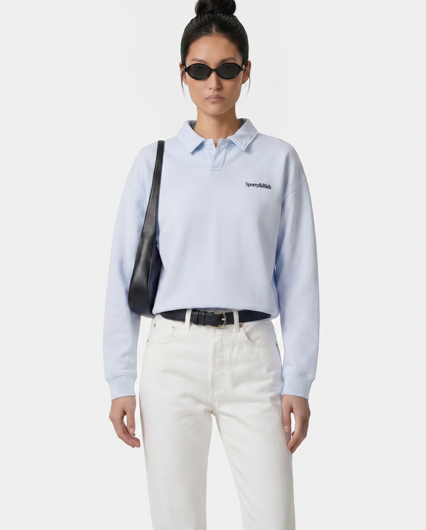Person wearing a light blue polo shirt with a brand logo, white pants, and carrying a black bag on a white background.