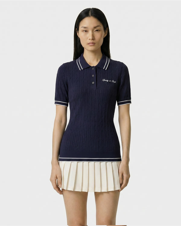 Woman wearing a navy polo shirt with white trim and a striped skirt on a white background