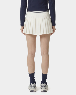 Person wearing a navy sweater, white pleated skirt, and dark socks on a white background