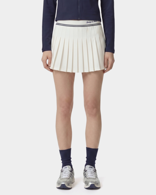 Person wearing a navy jacket, white pleated skirt, and gray sneakers on a white background