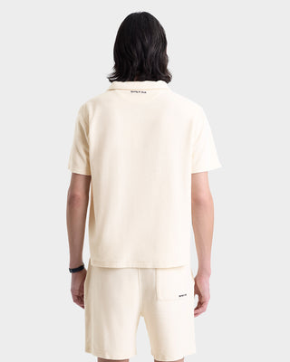 Person with shoulder-length dark hair wearing the Eden Script Terry Polo in Cream/Navy, seen from behind.