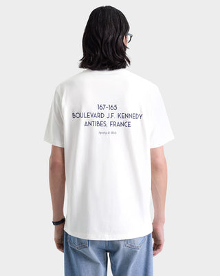 Person with long dark hair and glasses shown from behind wearing the Kennedy Crest T-Shirt in White/Navy, an oversized 100% cotton tee with text printed on the back.