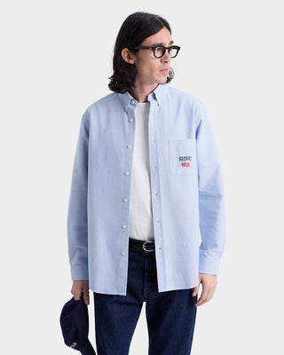 Person wearing a light blue button-up shirt with a logo on a white background