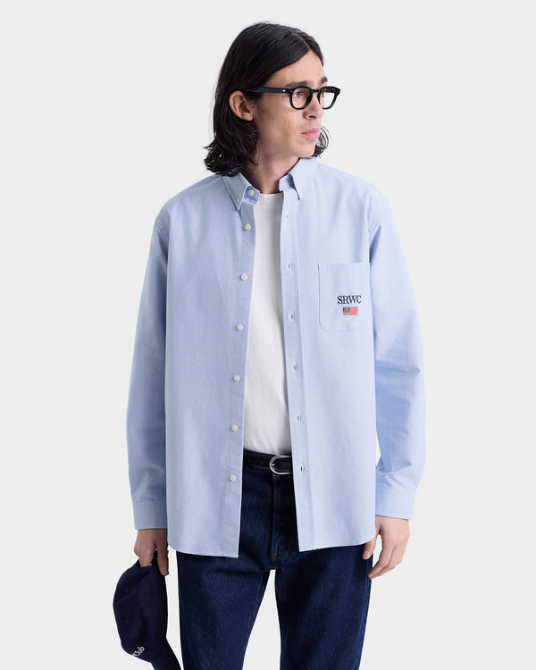 Person wearing a light blue button-up shirt with a logo on a white background