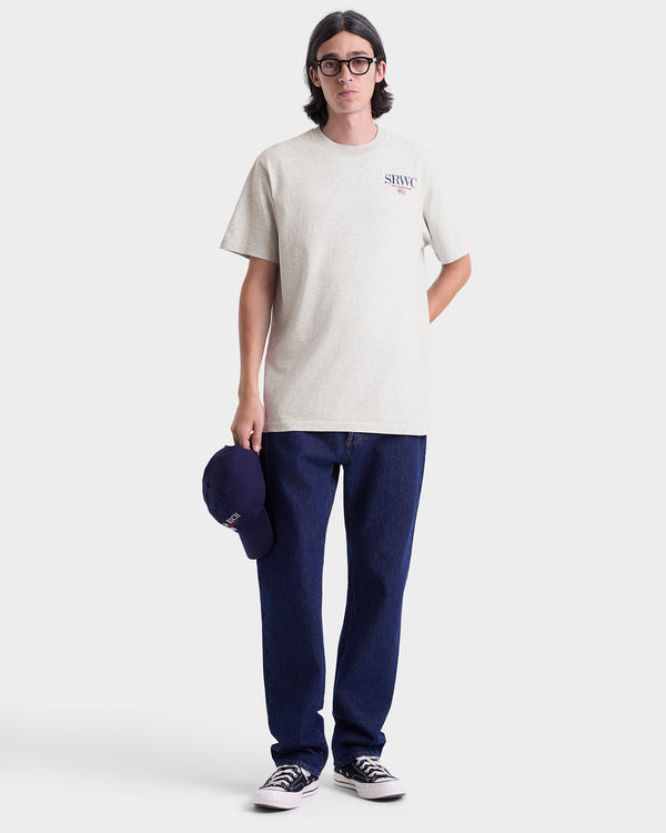 Person wearing a gray t-shirt and blue jeans holding a cap on a white background