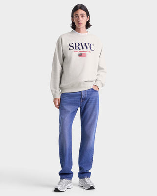 Person wearing a beige sweatshirt with 'SRWC' logo and blue jeans on a white background