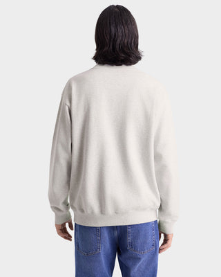 Person wearing a beige sweatshirt and blue jeans on a white background